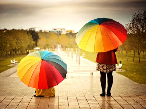 2 mensen met kleurrijke paraplu kijken naar zonnige wolken op een stenen park